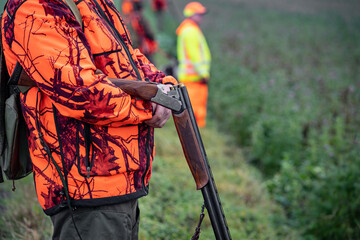 Sicherheit bei der Jagd: Jäger wartet am Feldrand mit nicht schußbereiter Waffe und in Signalkleidung. - obrazy, fototapety, plakaty