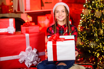 Obraz na płótnie Canvas Happy little smiling girl with christmas gift box. xmas mood. family holiday. kid in shopping mall. happy new year. child in red santa hat. kid with present box. winter shopping sale. magic gift box