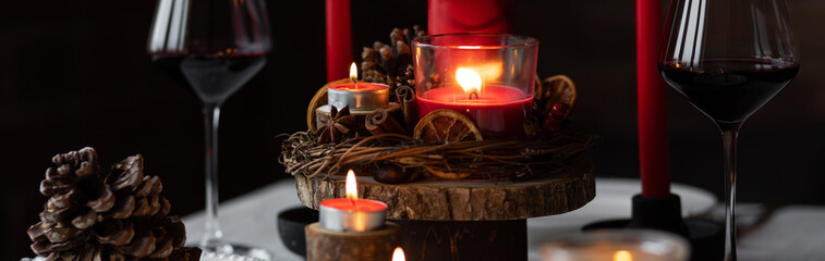 Rustic table decor for Christmas or New Year family dinner. Centrepiece with red candle, dry orange, cone, cinnamon, anise. Zero waste eco-friendly home. Cozy atmosphere, dark background. Banner