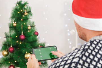 A man in Santa hat holds a phone in a horizontal position with a green screen. Phone with...