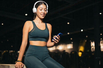 A young Japanese woman rests sitting on a wooden cube, the girl uses the mobile phone while listening to music with wireless headphones, youth sport