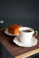 coffee and orange cake on a black background and porcelain tableware on a brown tapere