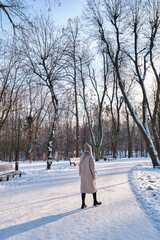 A woman walks in a winter park and enjoys a frosty sunny day. The concept of winter time and walks