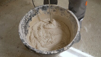 Mixing cement adhesive with a mixer in a bucket close-up, texture of a mixed mortar. A worker stirs the beige mixture in a bucket.
