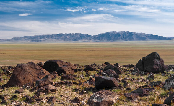 Steppenlandschaft mit Gebirge im Hintergrund und Steinbrocken im Vordergrund in der Mongolei, Zentralasien