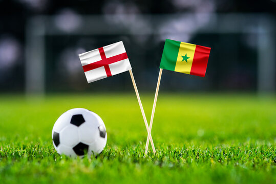 England - Senegal. Eight final, Last 16 football match. Handmade national flags and soccer ball on green grass. Football stadium in background. Black edit space.