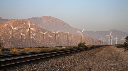 railroad tracks pass through a windmill farm as turbine tune to create energy