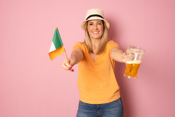 Young smiling woman holding a beer and irish flag standing isolated over pink background.