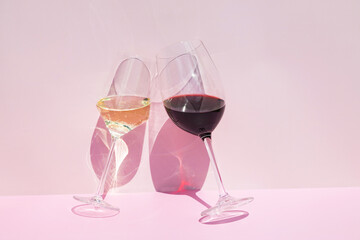 A glass of red and white wine on a pink background in the bright rays of the sun.