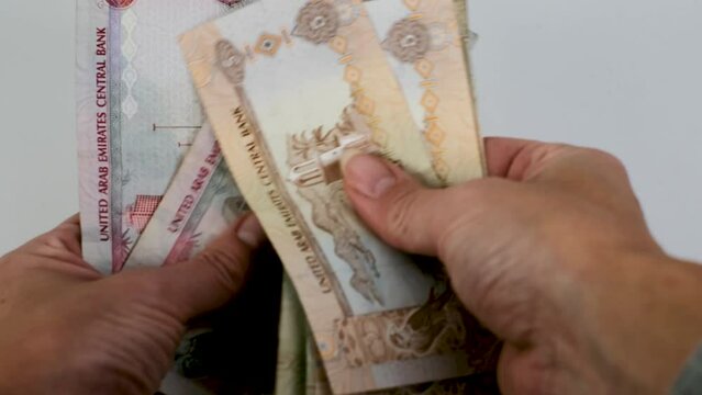 Hand counting United Arab Emirates dirhams on white background.