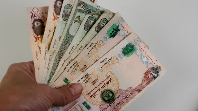 Hand counting United Arab Emirates dirhams on white background.