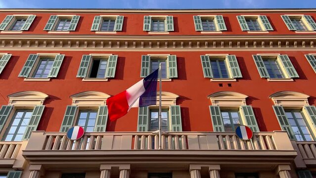 the flag of France waves on the classical facade of the building at sunset
