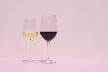 A glass of red and white wine on a pink background in the bright rays of the sun.
