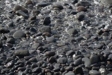 Water rolls into the ocean through large pebbles. Low tide. The water is seething. Texture, close-up.