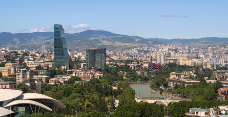 Aerial view on central part of the capital of Georgia Tbilisi Tiflis city with Mtkvari Kura river, two well-known high-rise buildings in the foreground and Vake-Saburtalo neighborhood climbing the © Vadim Rodnev