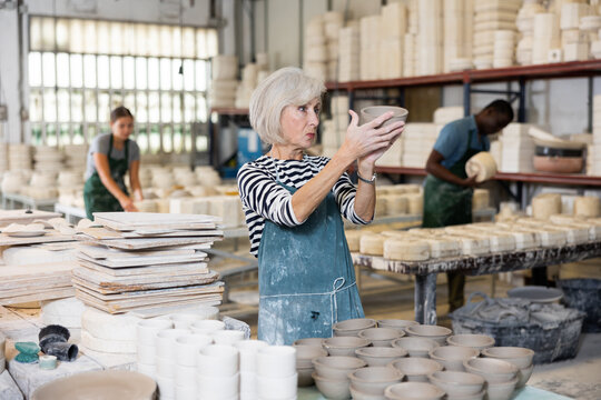 Portrait of positive senior woman holding ceramic cups at the workshop