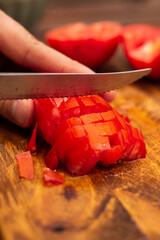 person cutting tomatoes into cubes on a piece of wood