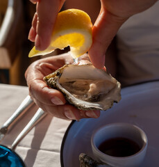 Young woman in white dress eats fresh live oysters with marinated onion, seafood in French restaurant