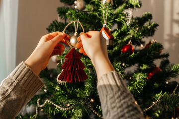 Close-up of the hands of a girl hanging a New Year's toy on a Christmas tree. Eve of Christmas and...