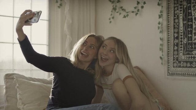 Girls sitting on bed posing for funny cell phone selfies / Highland, Utah, United States