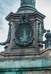 Copenhagen, Denmark - July 24, 2022: Ivar Huitfeldt Column detail. Bronze mural statue at bottom of Admirals brown stone column in Langelinie Park under blue cloudscape