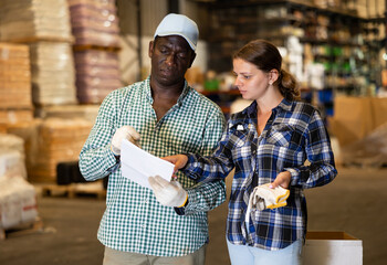 Positive African American man and woman checking order list at hardware store warehouse