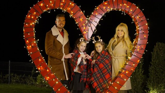 Young family posing for photo, while standing behing heart shaped Christmas decoration. Slow motion. 