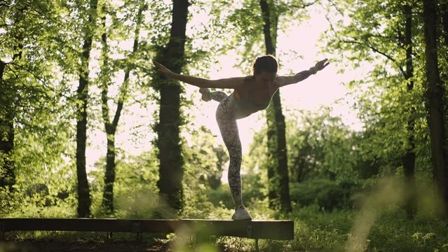 Young athletic woman doing yoga balancing pose in the sunny forest. Healthy lifestyle concept. Slow motion.