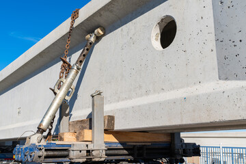 A large concrete beam secured by a hydraulic mechanism and chains to a car platform.