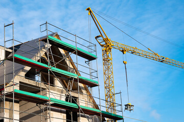 Top of an unfinished house with scaffolding. Construction crane against the blue sky.