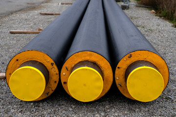 Three isolated heating pipes with yellow plastic plugs lie on a construction site.