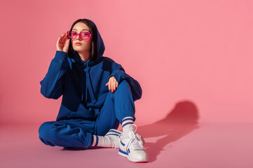 Young confident brunette woman wearing trendy blue suit with hoodie, trousers, pink color...