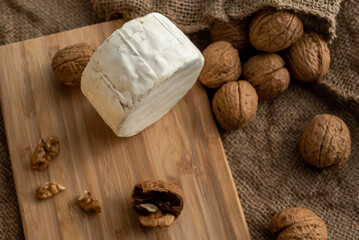 Composition of a round head of cheese with white mold and walnuts on a bamboo board on a background of burlap