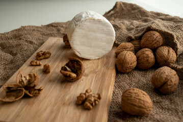 Composition of a round head of cheese with white mold and walnuts on a bamboo board on a background of burlap
