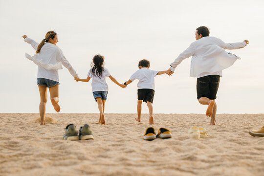 Happy family day. Back view of Asian having family parents with child fun holding hands together running to beach, lifestyle father, mother and kids relax take off shoes run on sand, holiday travel