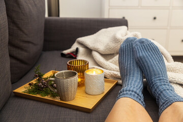 Soft photo of a woman`s legs in woolen blue socks on the sofa with a book and cup of tea and a...
