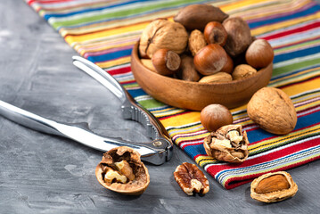 Various nuts in a wooden bowl on gray table and a nut cracker.  Close-up of a walnut. Space for text.