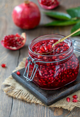Homemade canned pomegranate seeds with pomegranate juice in a glass jar and spoon full of seeds on top. Wooden table, selective focus, vertical.