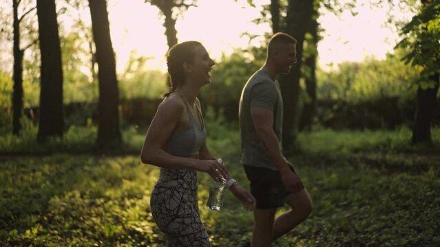 Couple walking and drinking water after the workout in the forest. Two people talking. Healthy lifestyle concpet. Slow Motion. 