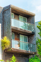 Modern house facade with slatted timber walls and glass balcony railings in partial sun