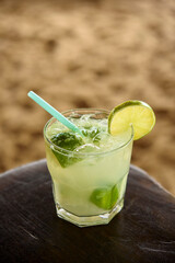 Brazilian caipirinha drink on wooden table with sandy beach background.