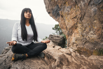 Young woman meditating and breathing on top of a mountain and forest