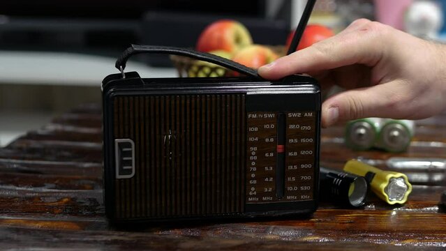 A man tunes a radio wave on the radio on an old wooden table. Antique receiver with antenna. Tune analog radio on a scale. A man listens to the news on an old radio. listening to music.