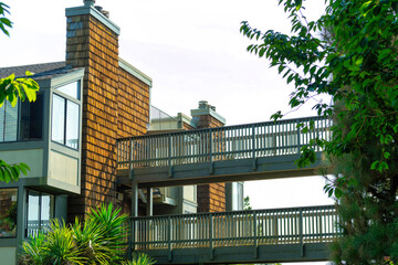 Modern housing complex with timber double bridges with slatted wood walls and white stucco with trees and plants in foreground