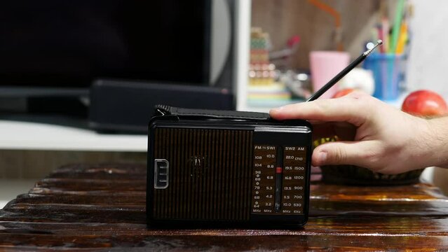Tunes a radio wave on the radio on an old wooden table. Antique receiver with antenna. Lifestyle. Tune analog radio on a scale. A man listens to the news on an old radio. listening to music