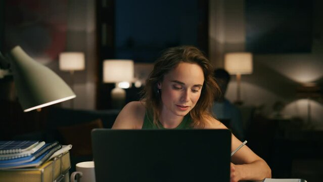Focused girl speaking computer at cozy home. Freelancer working laptop overtime
