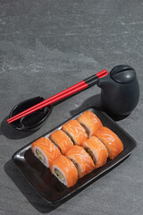 Sushi rolls with salmon, avocado and cucumber on a black rectangular plate on a black stone (slate) background.