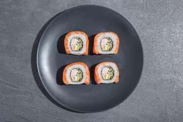 Sushi rolls with salmon, avocado and cucumber on a black round plate on a black stone (slate) background.