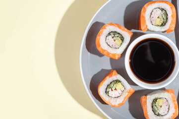 Fototapeta na wymiar Japanese sushi with salmon, dragon rolls on a bright yellow background. Pop art. Tasty snacks on a gray plate and chopsticks.