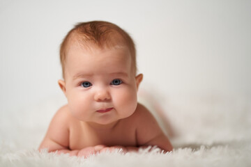 portrait of an infant with serious emotion lying on his belly against a white background